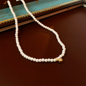 Détail d'un collier de perles vintage français avec un petit pendentif rond doré