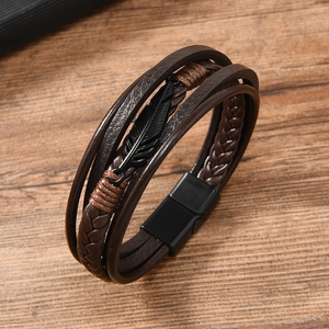 Close-up of men's layered brown braided leather bracelet with black feather charm and magnetic clasp
