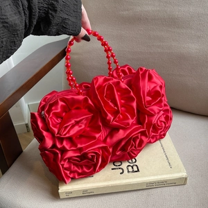 Detail of red silk rose clutch bag with beaded handle resting on an English book