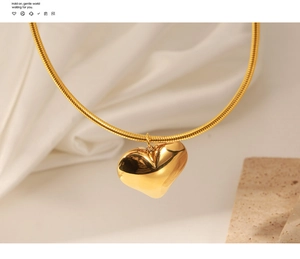 Macro view of a gold heart pendant on a snake chain over a marble pedestal