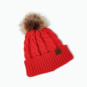 Detailed knit texture of red cable knit beanie with brown faux fur pom and leather label