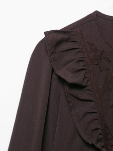 Détail d'une chemise marron foncé avec volants et broderies florales de précision