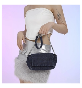Modella con una borsa in denim scuro con patta, cuciture a rombi e tracolla a catena argentata