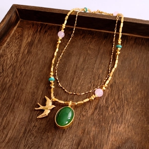 Gros plan détaillé du collier double rang doré avec pendentif vert et breloque oiseau