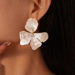 Close-up of model wearing white resin flower earrings with sparkling rhinestone details