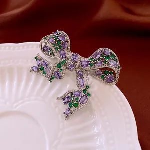 Bowknot brooch with purple and green zircon crystals on a vintage ceramic plate