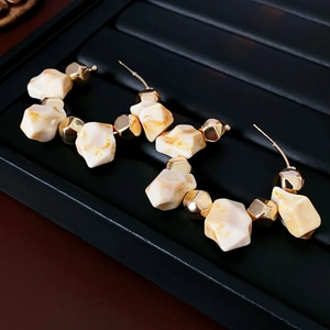 Detail of C-shaped hoop earrings with cream resin stones and faceted gold beads