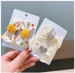 Detailed view of polka dot bow hair clips with yellow pom poms and rhinestone hearts