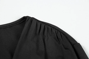 Detailed view of black V-neck dress featuring elegant pleated shoulders and premium fabric