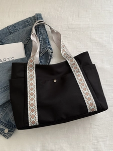 Dettaglio della borsa tote in tela nera con tracolla etnica e oggetti di scena artistici