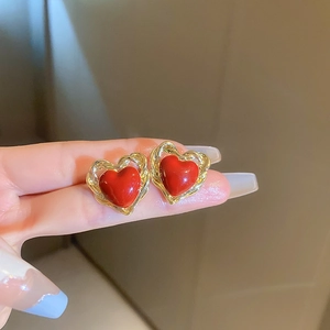 Detail showing hand holding gold-rimmed red heart stud earrings in resin with glossy finish