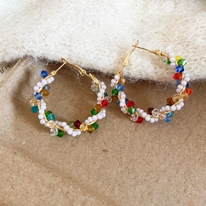 Detail of handmade gold hoop earrings with colorful crystal beads and white faux pearls