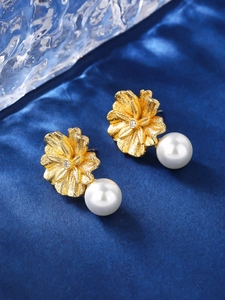 Macro shot of elegant golden flower earrings with white pearl and sparkling zircon center