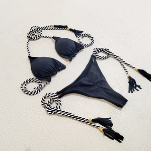 Flat lay of black bikini with decorative woven ropes, gold hardware and tassels detail