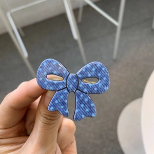 Detailed close-up of blue polka dot denim bow hair clip with golden metal duckbill clamp