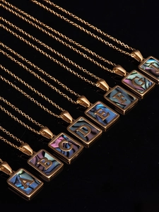 Macro shot of gold square alphabet pendants with colorful shell inlay on black backdrop