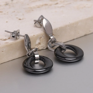 Detail of silver stainless steel earrings with black ceramic hollow circles on stone base