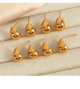 Macro view of gold teardrop earrings and curved stud sets in a beige jewelry box