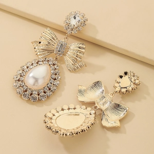 Close-up of gold bow earrings with crystal diamonds and large drop-shaped pearls