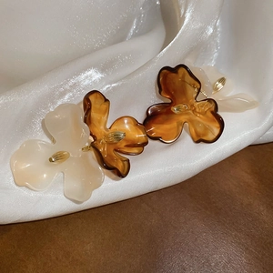 Detail shot of acrylic flower earrings in cream and amber with silk and wood background