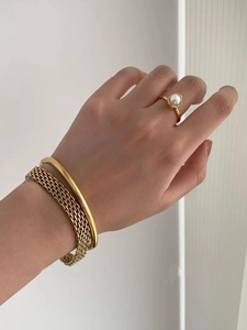 Close-up of gold titanium steel bangle with woven metal texture and pearl ring on model
