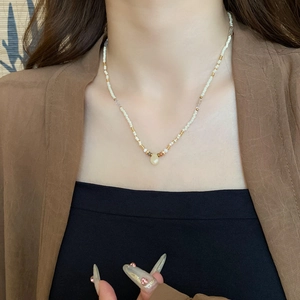 Close-up of white beaded necklace with gold accents and a translucent teardrop pendant