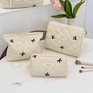 Close-up of three cream quilted makeup bags with embroidered bows and metal zippers
