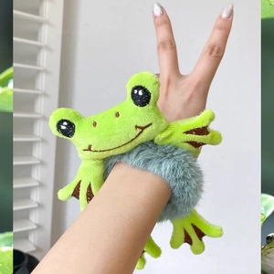 Cute green plush frog hair ring scrunchie worn on wrist with vibrant natural lighting