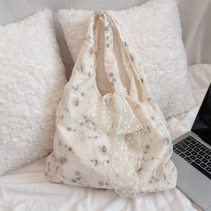 Detail of floral embroidery and large lace bow on a cream canvas shoulder tote bag