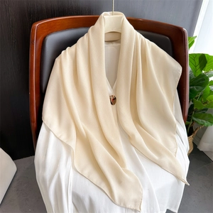 Detail of a beige linen scarf styled over a white shirt with a decorative metal buckle