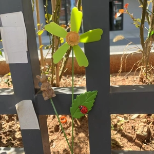 Dettaglio picchetto da giardino con fiore verde, viso sorridente e scoiattolo marrone