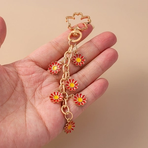 Detail of daisy flower keychain with red and yellow enamel petals held in a hand