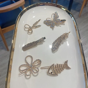 Close-up of gold metal hair clips with rhinestones in shapes like scissors and feathers
