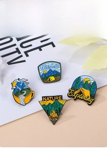 Detail of four enamel outdoor adventure pins with mountains, campfire, and forest designs
