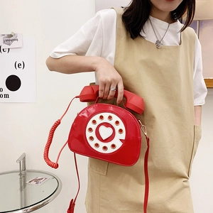 Detail of red patent leather crossbody bag in creative vintage telephone shape with handset handle