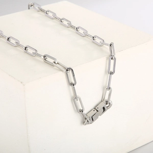 Detail of silver paperclip link chain with a geometric mechanical clasp on white blocks