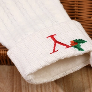 White knitted Christmas stocking with red letter A embroidery and green holly leaves decoration