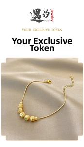 Detail of gold beads bracelet with textured charms on a soft champagne silk backdrop