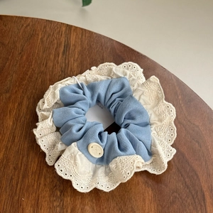 Blue floral scrunchie with lace edge and decorative button on a dark wood table