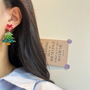 Close-up of handmade beaded Christmas tree earrings with a red bow on a female model