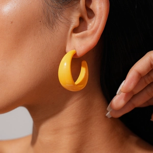 Close-up of a model wearing bright yellow C-shaped resin earrings in a chunky vintage style