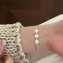 Detailed view of silver bracelet featuring triple rose pendants on a knit sweater sleeve