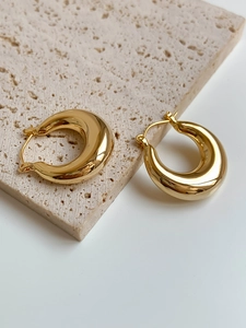 Close-up of chunky gold hoop earrings on a beige stone slab with a polished mirror finish