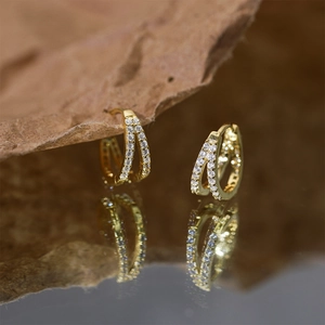 Macro detail of gold S925 silver cross hoop earrings with cubic zirconia on mirrored base