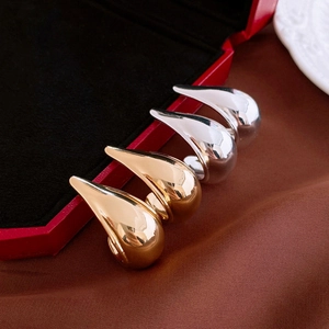 Elegant gold and silver metallic teardrop stud earrings on brown satin fabric