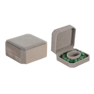 Gray velvet octagonal jewelry box displaying a green bracelet inside on a white background