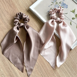 Detail of mocha and champagne satin hair scrunchies with long ribbons on wooden surface