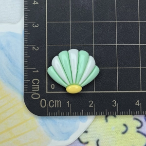 Macro detail of a 2cm green and white resin seashell charm on a measurement scale mat