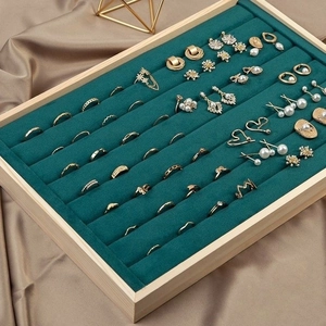 Dark green velvet jewelry tray with wooden frame displaying gold rings and pearl earrings