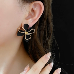 Detailed view of layered 3D flower earrings in black and gold on model's ear